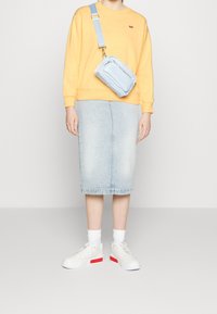 Sudadera amarilla, bolso cruzado azul claro, falda lápiz de mezclilla clara, zapatillas blancas con detalles rojos y calcetines tobilleros blancos.