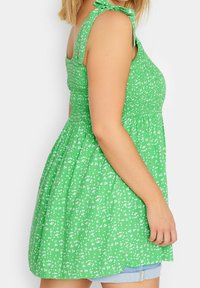 Vestido verde con estampado floral, cuerpo fruncido y tirantes con lazos. Tejido ligero, falda acampanada con pequeñas flores blancas por todo el vestido.