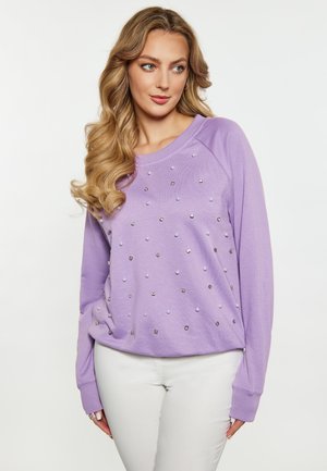 Sweatshirt lilas clair avec perles argentées et nacrées, col rond, poignets côtelés et coupe décontractée. Associé à un pantalon blanc.