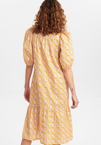 Vestido midi floral em tons pastel de rosa, laranja e amarelo. Apresenta mangas bufantes e uma bainha em camadas com um corte solto e tecido natural.