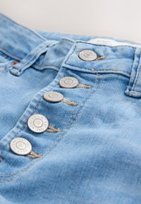 Világoskék farmernadrág gombos záródással, négy fém gombbal, látható varrással és sima textúrával.