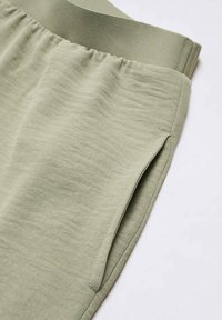 Pantalons de sport vert clair avec un tissu texturé, une taille élastique et des poches latérales. Design simple, sans motifs ni accents supplémentaires.