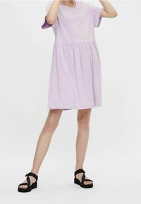 Liliowa bawełniana sukienka z krótkimi rękawami, marszczoną talią i spódnicą do kolan. W zestawie z czarnymi sandałami na platformie. Gładka tekstura.