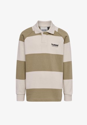 Dziecko z długimi blond włosami, ubrane w beżowe i białe paskowane polo, granatowe spodnie dresowe i białe trampki, stojące na jednolitym tle.