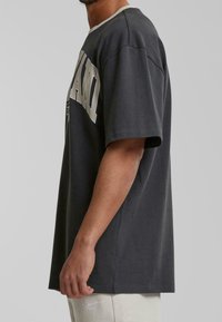 Gray oversized t-shirt with short sleeves, round neckline, and large white text graphic on the front. Smooth cotton fabric, relaxed fit.