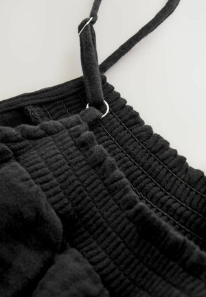Schwarzes, strukturiertes Stoffkleidungsstück mit Rüschendetails und verstellbaren Trägern. Verfügt über silberne Beschläge zur Einstellung der Träger.