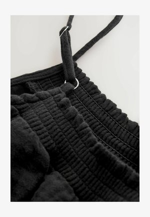 Haine din țesătură neagră texturată cu margini volanate și bretele ajustabile. Include detalii din metal argintiu pentru ajustarea bretelelor.