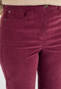 Bordeaux corduroy broek met een zachte textuur, voorzien van zijzakken, een knoopsluiting en subtiele ribbelpatronen.
