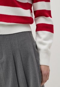 Rot-weißer gestreifter Strickpullover mit gerippten Bündchen, kombiniert mit hoch taillierten, grauen, strukturierten, gefalteten Hosen.