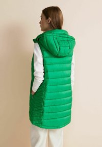 Zelená nafukovací vesta s kapucí, která má horizontální a chevronové prošívané vzory. Vyrobena z lesklého materiálu, má boční kapsy a zapínání na zip.