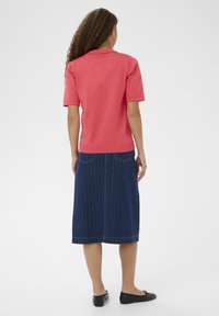 Polo rose à manches courtes associé à une jupe en denim bleu foncé avec des rayures verticales et une couture à l'ourlet. Des chaussures plates noires sont portées.