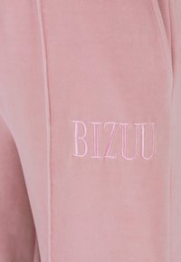 Roze velours joggers met een geborduurd "BIZUU" logo in bijpassende draad, met een zachte textuur en gestroomlijnd ontwerp.
