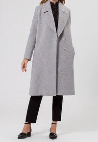 Cappotto di lana grigio con ampi revers e una texture morbida. Caratterizzato da quattro bottoni e una silhouette dritta. Abbinate con pantaloni e scarpe nere.