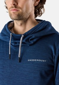 Felpa blu con cappuccio realizzata in un tessuto testurizzato, dotata di un ampio collo a camino, lacci grigi e un logo bianco "SWEDEMOUNT" sul davanti.