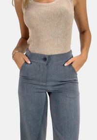 Débardeur beige à côtes associé à un pantalon gris taille haute avec une fermeture à bouton et des poches latérales. Texture de tissu lisse.