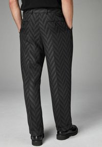 Pantalons noirs à motifs avec un design en chevrons, dotés d'un devant plat, de poches latérales et d'une coupe décontractée. Poignets fuselés et texture lisse.