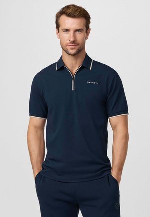 Polo azul marino con cuello de cremallera, ribete blanco contrastante y logo bordado. Tejido suave con mangas cortas. Se lleva con pantalones a juego.