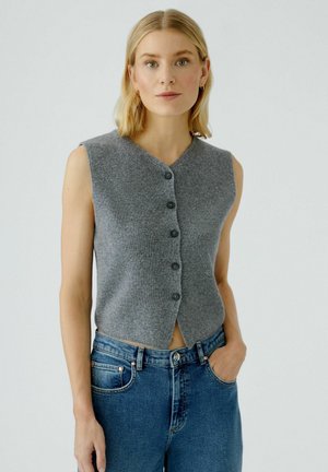 Grauer ärmelloser, cropped Pullover mit V-Ausschnitt und fünf schwarzen Knöpfen, kombiniert mit hoch taillierten blauen Jeans. Flach gestrickte Textur.