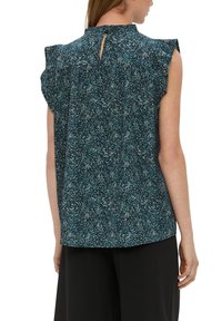 Blaue Bluse mit Muster und Rüschenschößchen, Knopfverschluss am Rücken und lockerer Passform, aus leichtem Stoff mit strukturierter Optik.