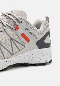 Bottines de sport gris clair avec une tige en mesh, accents gris, semelle intermédiaire blanche mouchetée et détails orange. Présente un design texturé pour l'adhérence.