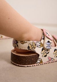 Sandale à imprimé floral avec une tige synthétique beige, des accents de bride roses et une semelle texturée imitation liège. Dotée de brides réglables pour un ajustement parfait.