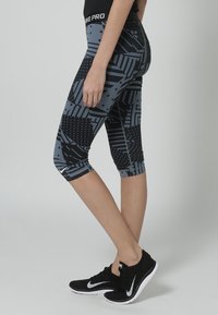 Legginsy Nike Pro capri w czarno-szarym geometrycznym wzorze. Wykonane z elastycznego materiału, posiadają talię o średnim stanie i skróconą długość.
