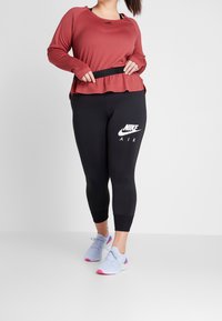 Rode lange mouwen top met een pijlrokontwerp, gecombineerd met zwarte leggings met een wit Nike-logo. Lichtblauwe sportschoenen met roze accenten.
