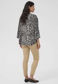 Bunt gemusterte Bluse mit Leopardenprint und weiten, lockeren Ärmeln, kombiniert mit beigen, figurbetonten Hosen und schwarzen, durchlöcherten Ballerinas.
