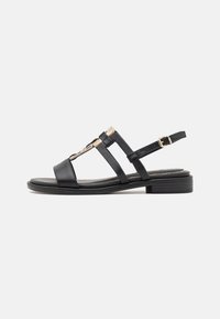 Black leather sandal featuring multiple straps, a low block heel, and a gold accent on the toe area. Adjustable buckle closure at the back.