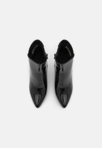 Bottines en cuir verni noir avec des pointes effilées et un design épuré. Présentent une texture lisse et des fermetures éclair sur le côté pour un enfilage facile.