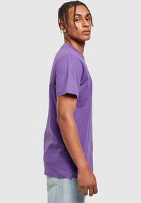 Camiseta de algodón morada con mangas cortas, cuello redondo y corte estándar. La vista muestra el perfil lateral del modelo. Diseño sencillo sin patrones.