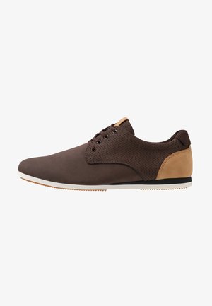Chaussure décontractée marron à lacets avec côtés perforés, patch au talon couleur fauve, semelle blanche et bande de roulement couleur gomme, vue de côté extérieur.