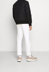 Schwarze Bomberjacke, weiße steife Hose und beigefarbene Sneaker. Das Outfit weist ein einfaches Design mit einfarbigen Tönen und minimalen Akzenten auf.