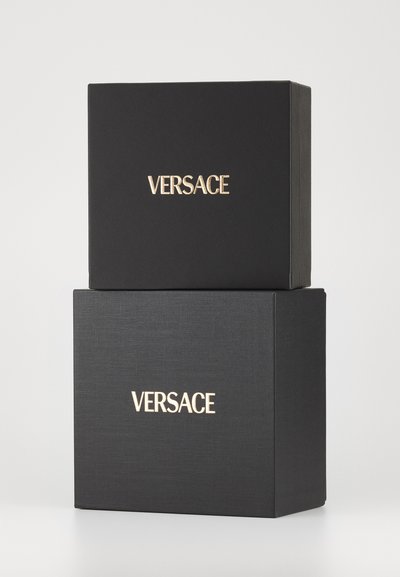 Black gift boxes stacked, featuring gold "VERSACE" branding. The texture is smooth with a subtle fabric-like pattern on the top box.