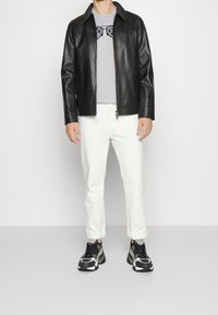 Chaqueta de cuero negra con cuello, camisa gris con gráfico de pajarita, pantalones blancos y zapatillas negras con estampado.