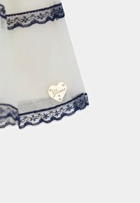 Tissu blanc transparent avec bordure en dentelle bleu marine à l'ourlet, ornée d'une étiquette en métal en forme de cœur embossée du mot "Guess" et de deux petits strass.