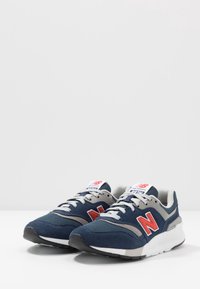 Marina sneakers med grå accenter, vit mellansula och röd branding. Har en texturerad mocka- och mesh-överdel, runda snören och vadderad krage.