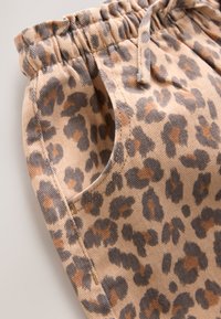 Gros plan sur un pantalon à taille élastique avec un motif léopard dans des tons beige, noir et marron.