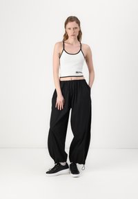 Hvit avkortet tanktop med svart trim, paret med løstsittende svarte bukser. Svart sneakers, elastiske mansjetter på buksene, enkelt design.