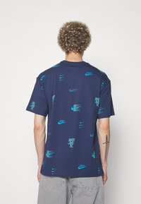 Tmavě modré bavlněné tričko s opakovanými tyrkysovými logy Nike a textem "JUST DO IT", krátké rukávy a klasický střih.