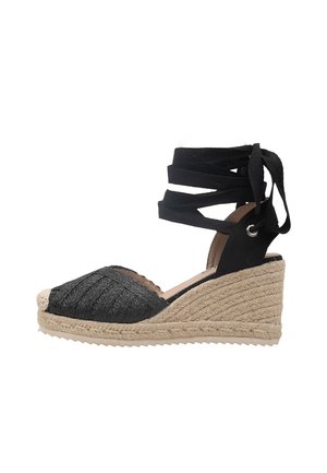 Sandalia alpargata negra con cuña, parte frontal tejida, tiras para atar en el tobillo y suela de yute trenzado natural.
