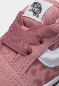 Κοντινή λήψη ενός ροζ αθλητικού παπουτσιού Vans με χονδρά κορδόνια, λευκή πλευρική ρίγα και το λογότυπο Vans Off The Wall στη γλώσσα.