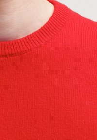 Czerwony sweter dzianinowy z prążkowanym okrągłym dekoltem, gładką fakturą i dopasowanym krojem, o jednolitej kolorystyce i starannych detalach.