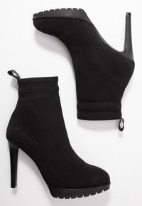 Stivaletti alla caviglia in stile calzino neri con alti tacchi a stiletto. Realizzati in un tessuto elasticizzato con un colletto a coste e un sottile marchio in rilievo sul lato.