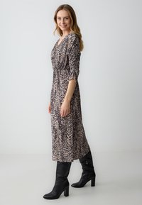 Leopardenmuster-Kleid mit V-Ausschnitt, taillierter Taille und Dreiviertelärmeln; ergänzt durch knielange schwarze High Heels.