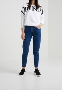 Vit sweatshirt med svart grafisk text, kombinerad med blå denimjeans. Skor: svarta sneakers med vit sula.