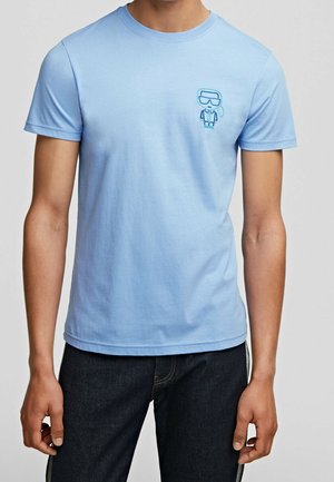 Jasnoniebieska bawełniana koszulka z okrągłym dekoltem, z małym haftowanym graficznym zdjęciem postaci w goglach po lewej stronie klatki piersiowej.