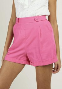 Shorts en coton rose à taille haute, avec des ourlets roulés, deux plis à l'avant et deux boutons décoratifs à la taille.