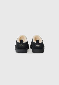 Svarta UGG-skor med en mjuk kr�ämfärgad foder, låg profil, rund tå och en liten dragflik baktill. Hållbar gummisula med logotypdetalj.
