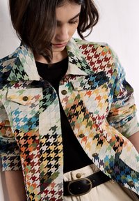 Chaqueta de denim con estampado de pata de gallo colorido que presenta tonos verdes, rojos y azules, con botones de latón y un cuello puntiagudo.